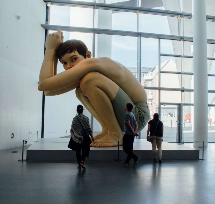 Giant art piece of a crouching shirtless and shoeless boy at ARoS