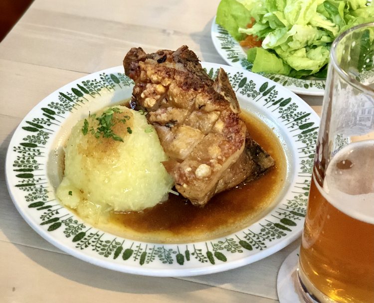 Schäufele on a plate with potato dumpling and gravy on a plate, a small salad in the background and a half empty glass of beer in the foreground - german food